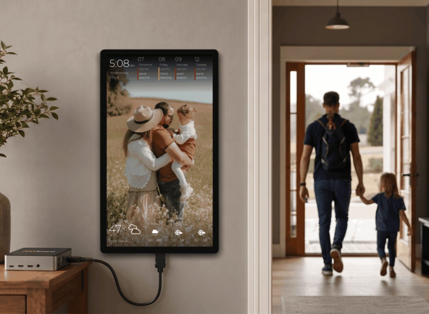 Portrait DAKboard wall display powered by a CPU Mini on a side table, showing a family photo, upcoming agenda, and weather forecast