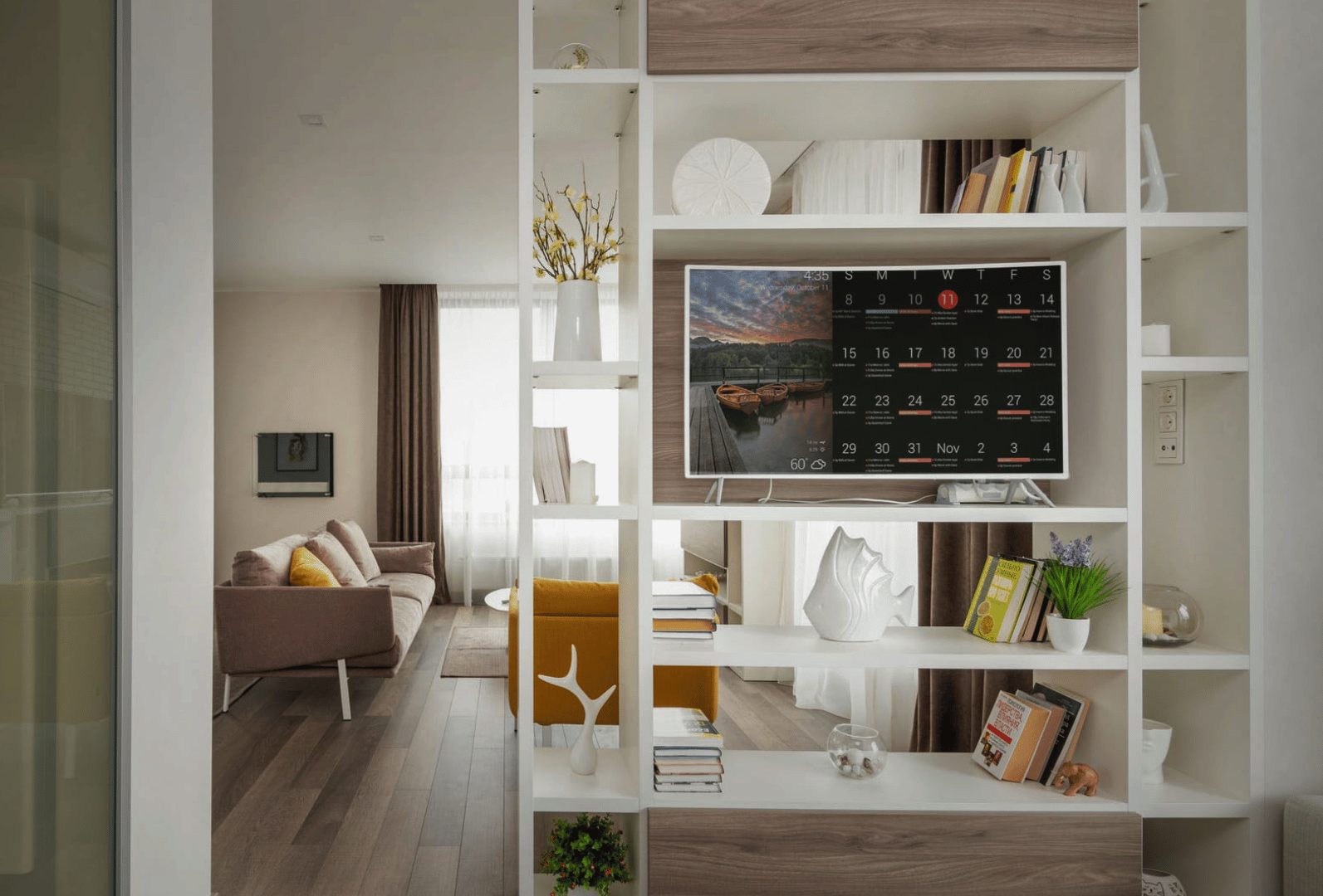 DAKboard on a large screen set into white living-room shelving, showing a monthly calendar beside a scenic lake photo widget