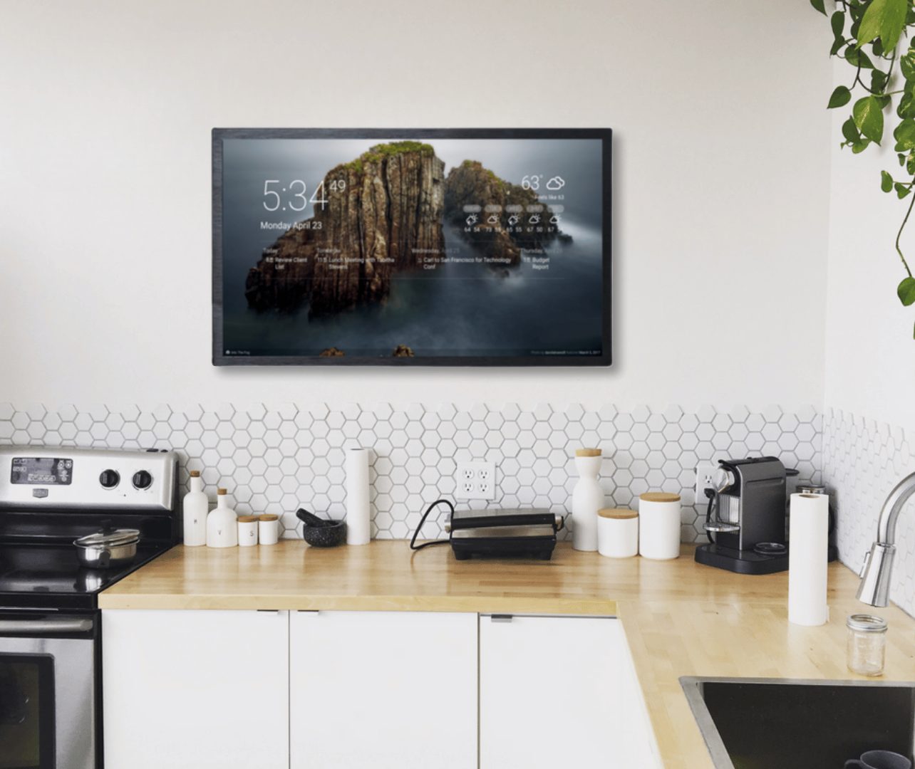 Travel photo dashboard Wall-mounted DAKboard in a white kitchen displaying a full-screen coastal travel photo with clock, agenda, and weather