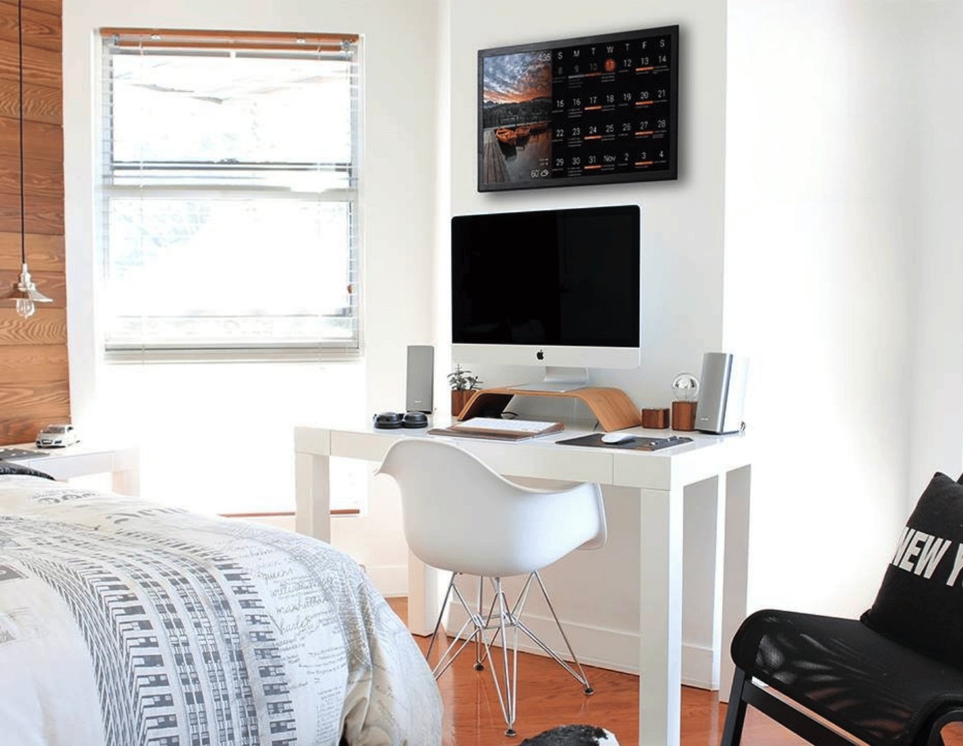 Color-coded family calendar Wall-mounted DAKboard above a bedroom desk showing a monthly photo calendar with color-coded events for each family member