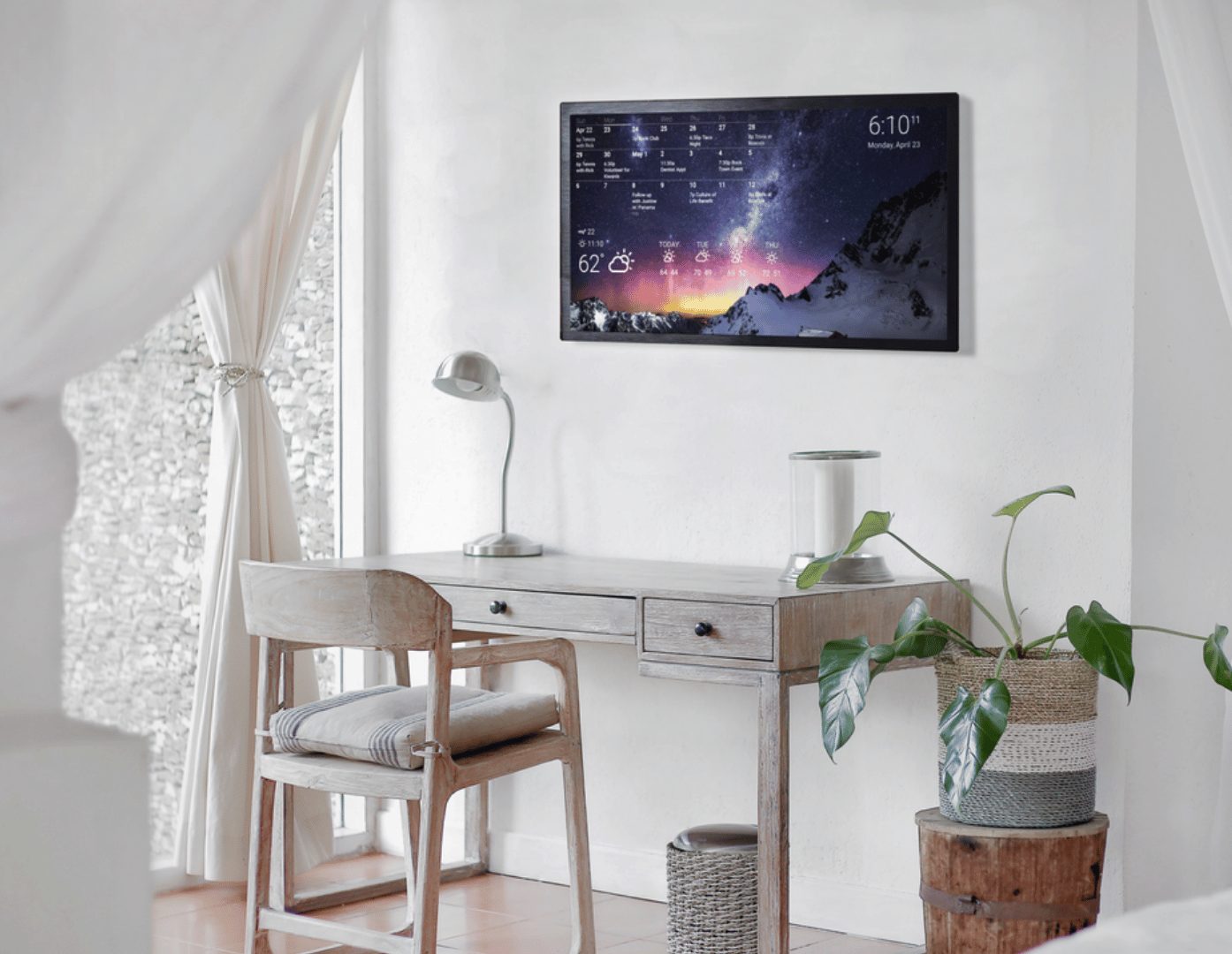 Minimalist wall calendar display Wall-mounted DAKboard in a bright minimalist room showing a monthly calendar and multi-day weather over a mountain photo