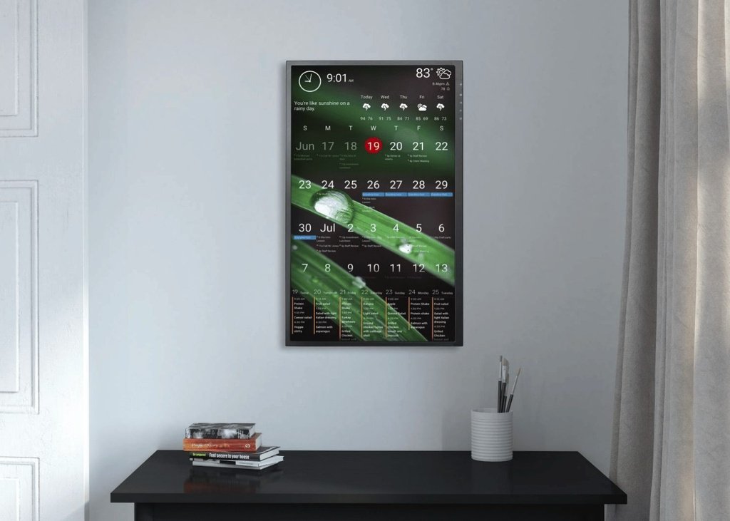 Portrait wall display A portrait wood-framed DAKboard wall display showing a monthly calendar and meal plan over a green nature photo